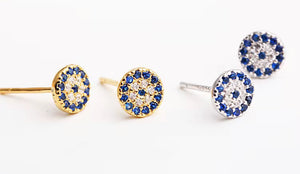 Sterling silver and gold-plated sterling silver evil eye stud earrings with blue and white cubic zirconia stones, protective talisman jewellery symbolizing luck and protection, displayed on a white background.