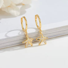 Load image into Gallery viewer, Pair of gold-plated sterling silver starfish huggie earrings with cubic zirconia, displayed on a white background with a book edge
