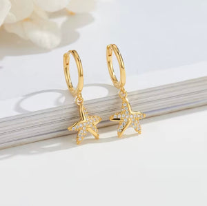 Pair of gold-plated sterling silver starfish huggie earrings with cubic zirconia, displayed on a white background with a book edge