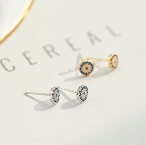 Sterling silver and gold-plated sterling silver evil eye stud earrings with blue and white cubic zirconia stones, protective talisman jewellery symbolizing luck and protection, displayed on a white background.
