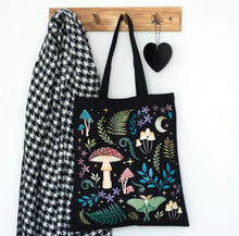 Load image into Gallery viewer, Black polycotton tote bag featuring a dark forest print with mushrooms, glowing luna moth, moon, and mystical plants.
