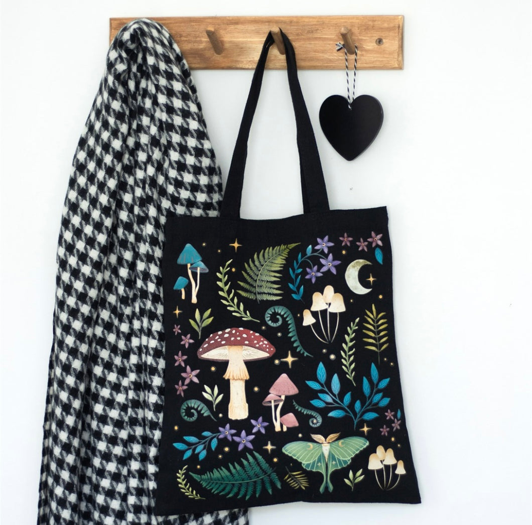 Black polycotton tote bag featuring a dark forest print with mushrooms, glowing luna moth, moon, and mystical plants.